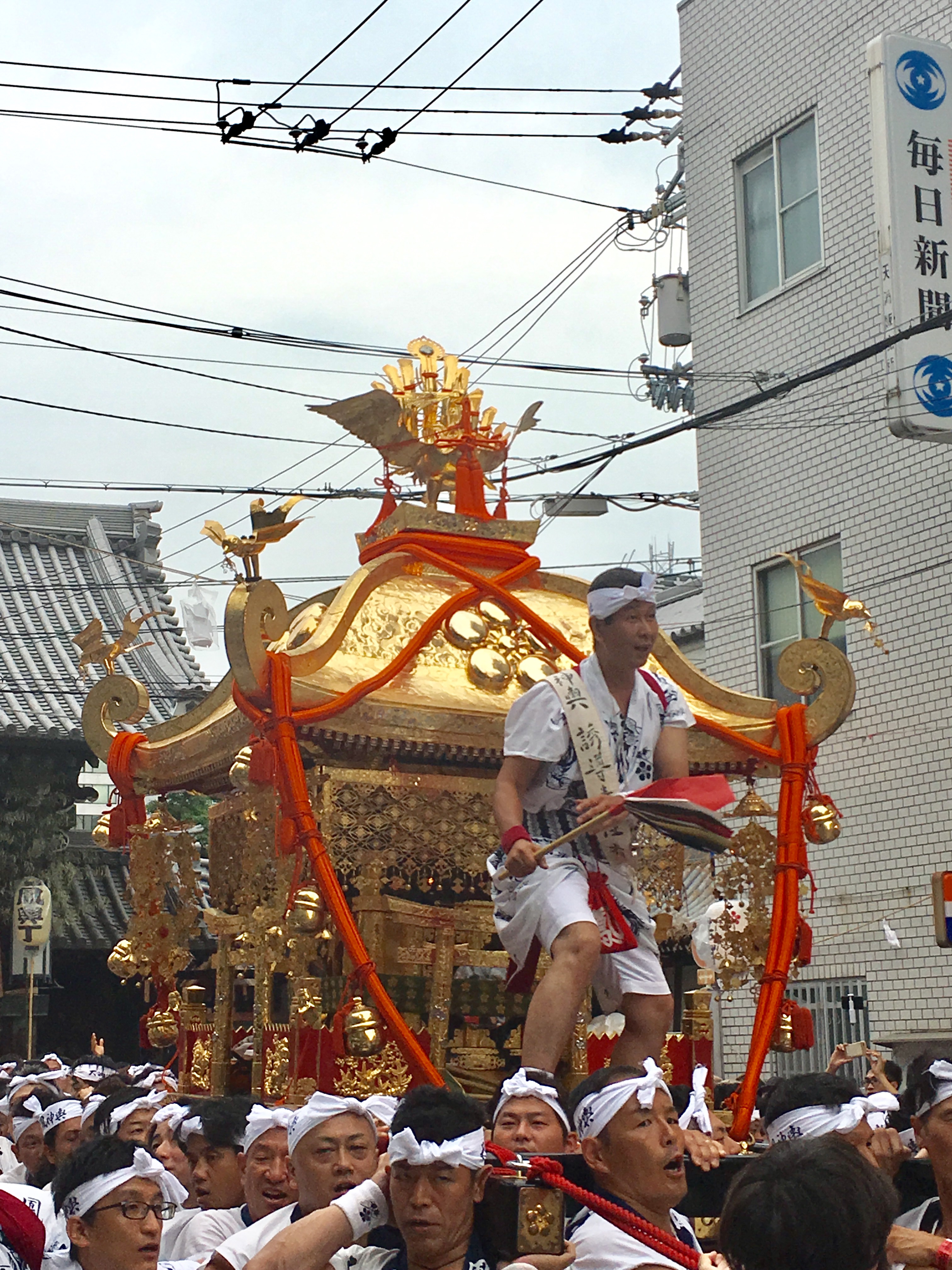 people riding large portable shrine through the street at tenjin matsuri