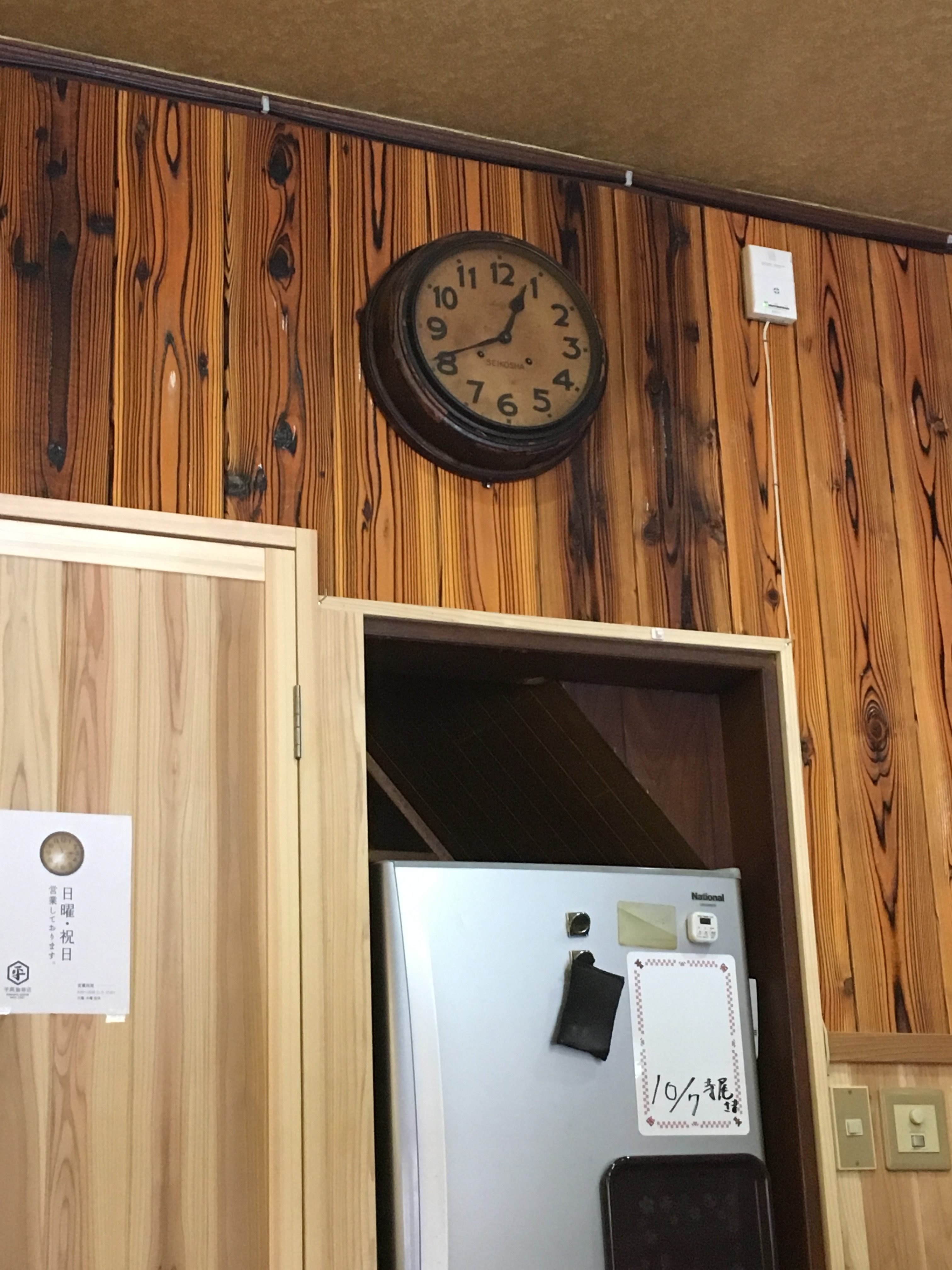 old clock against wood paneling above a refrigerator 