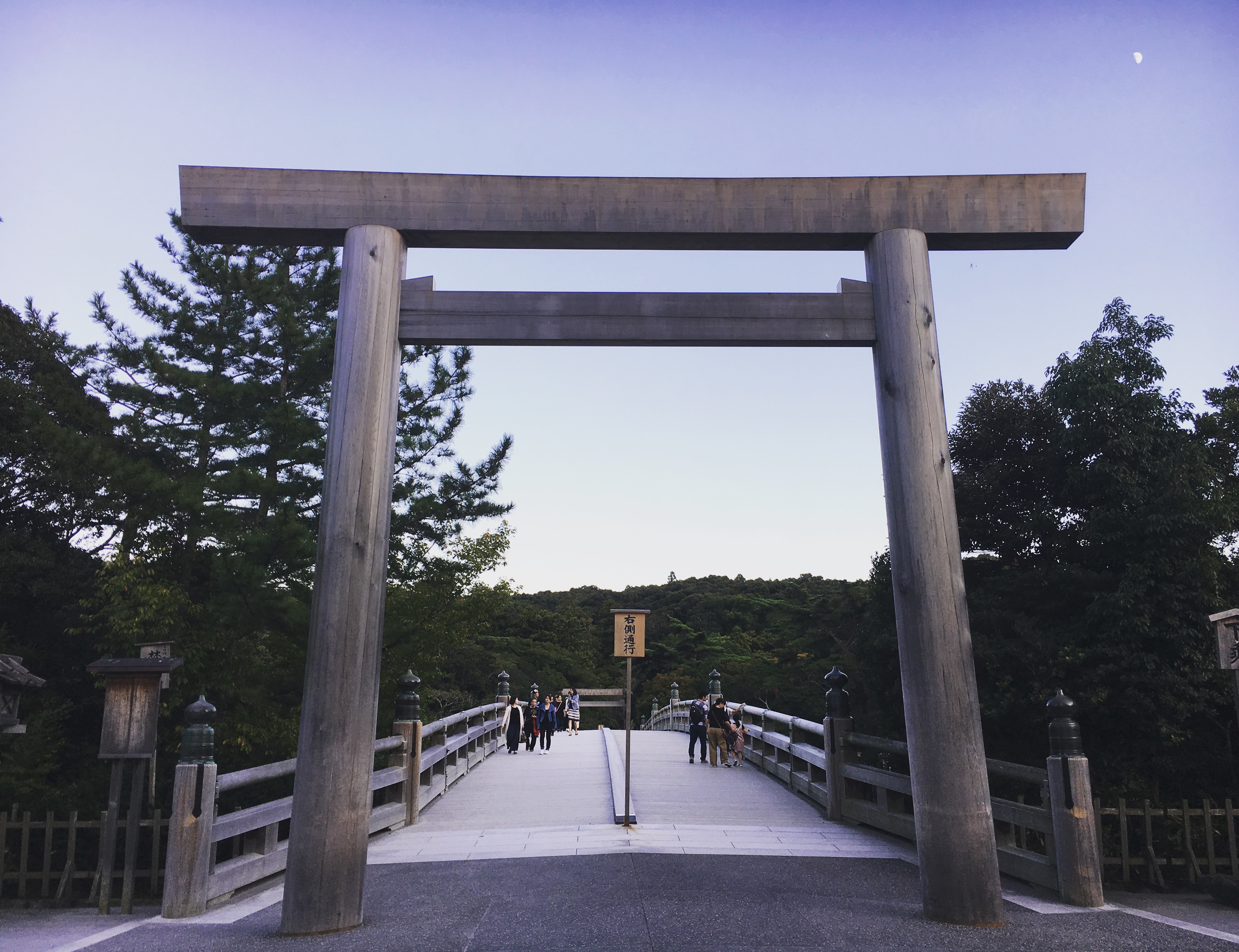 large wooden torii in front of long bridge at sunset