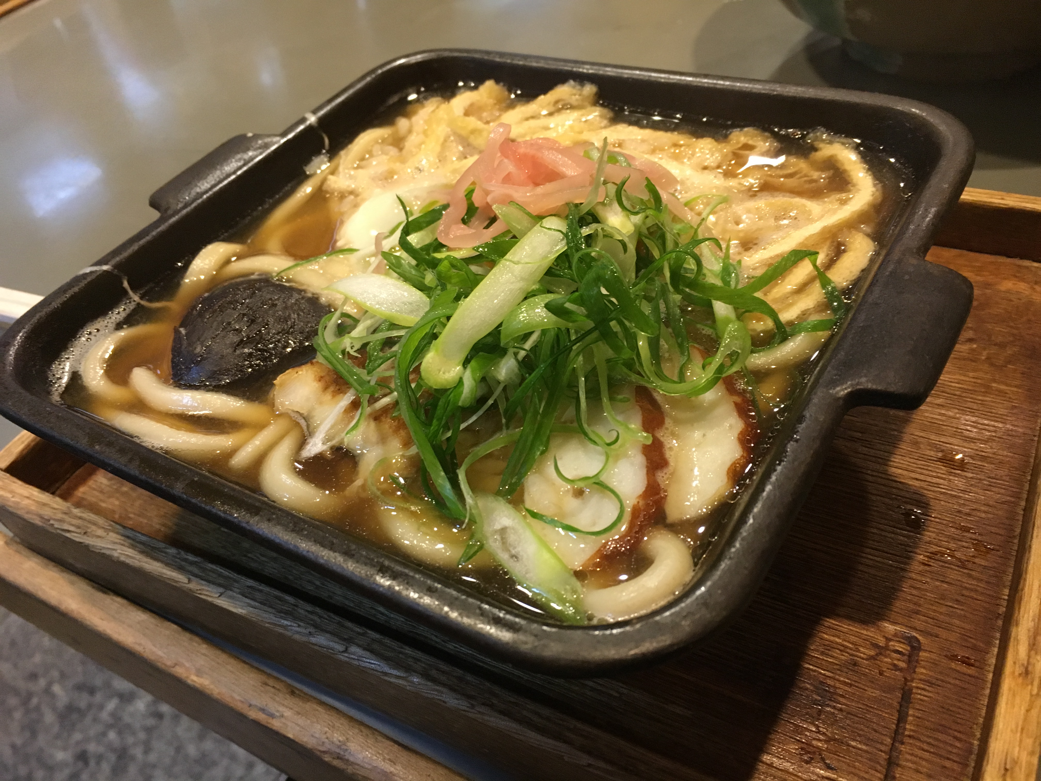 square cast iron dish containing a japanese dish of rice udon noodles broth and toppings
