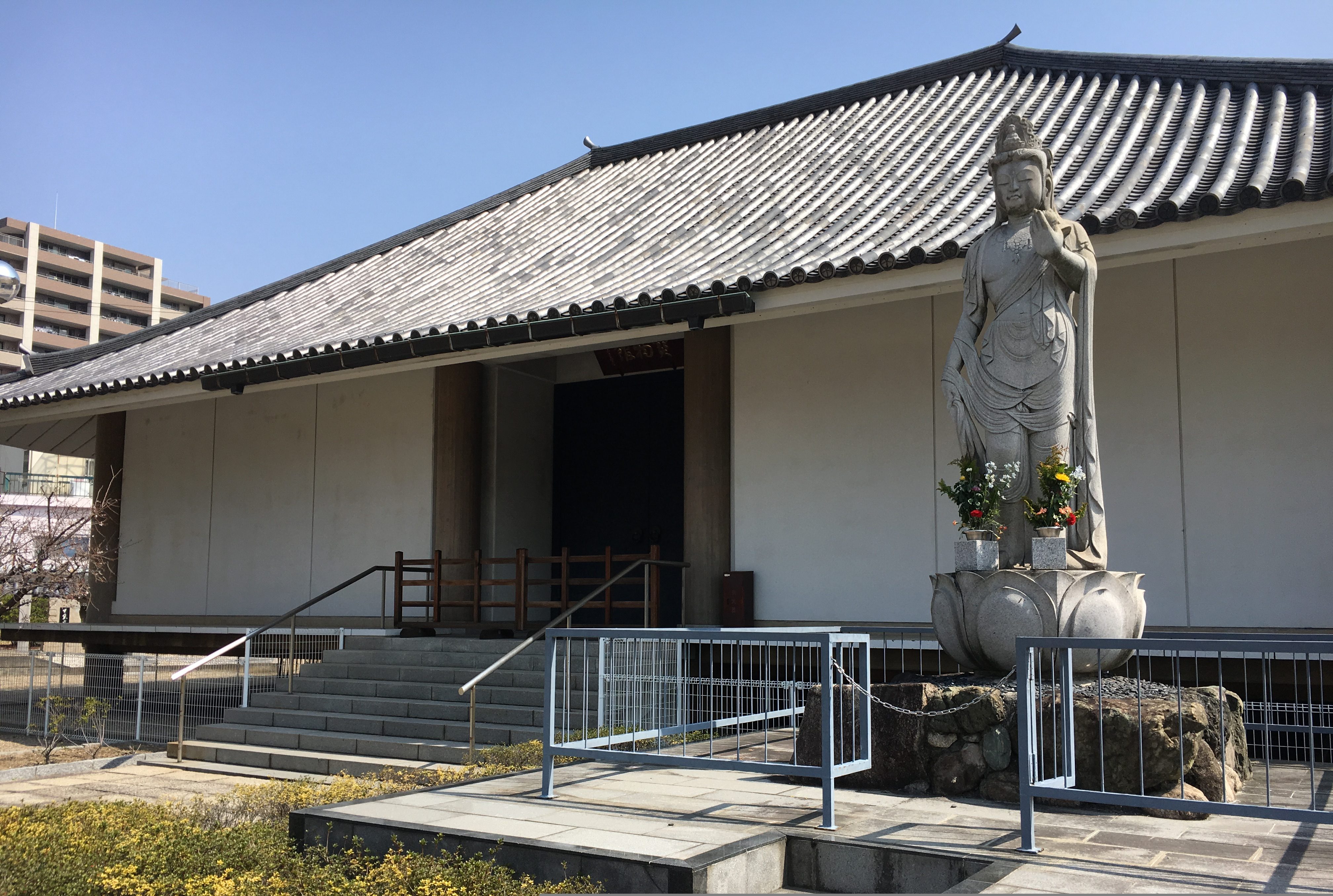 white building with Japanese tiles and a statue of Kannon Bosatsu in front of building