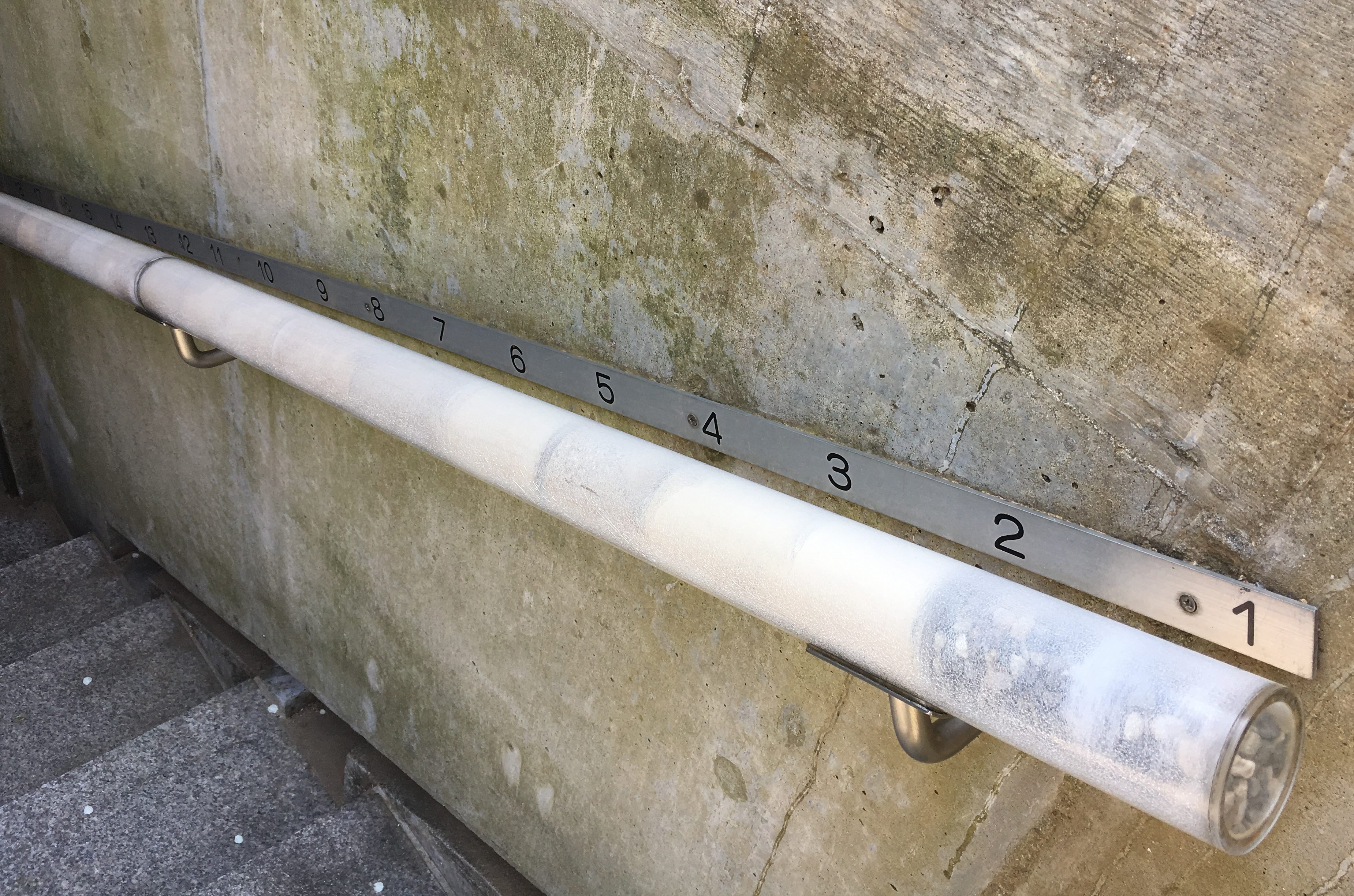 cement wall with a plastic railing filled with various kinds of sand