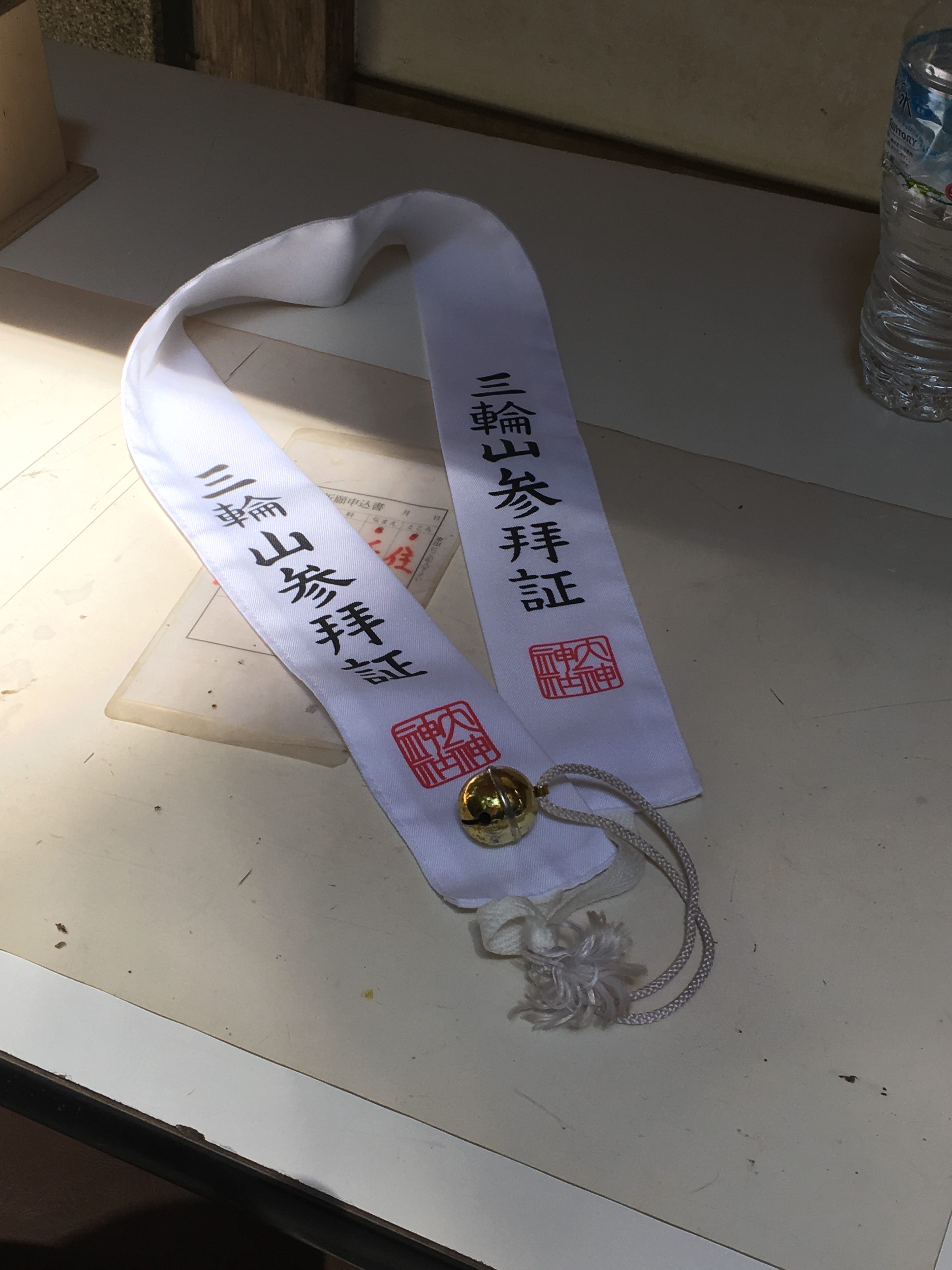 white sash with Japanese lettering and a bell on a white table 