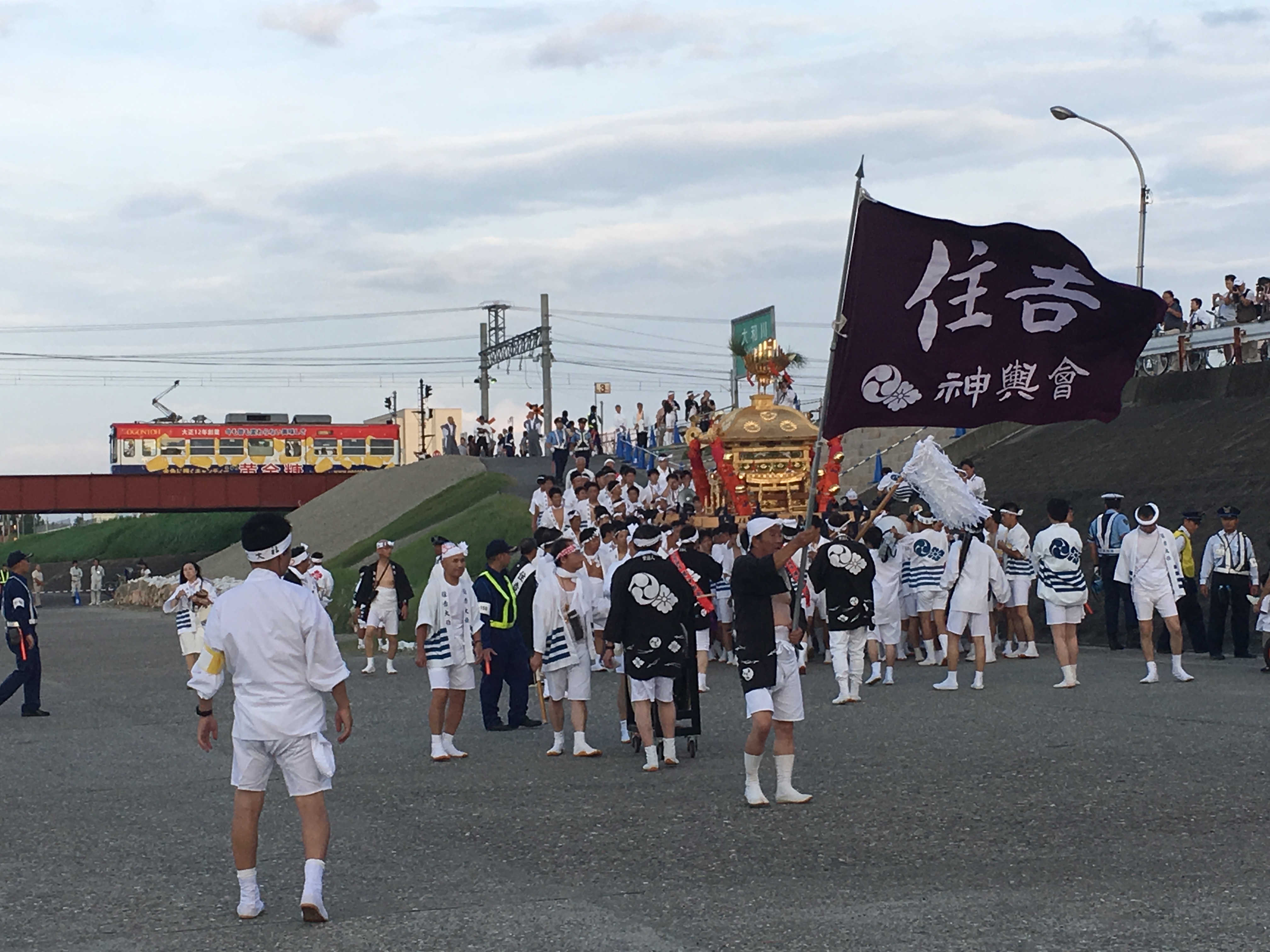 Sumiyoshi Matsuri participants meeting along the river side as a train passes in the distance