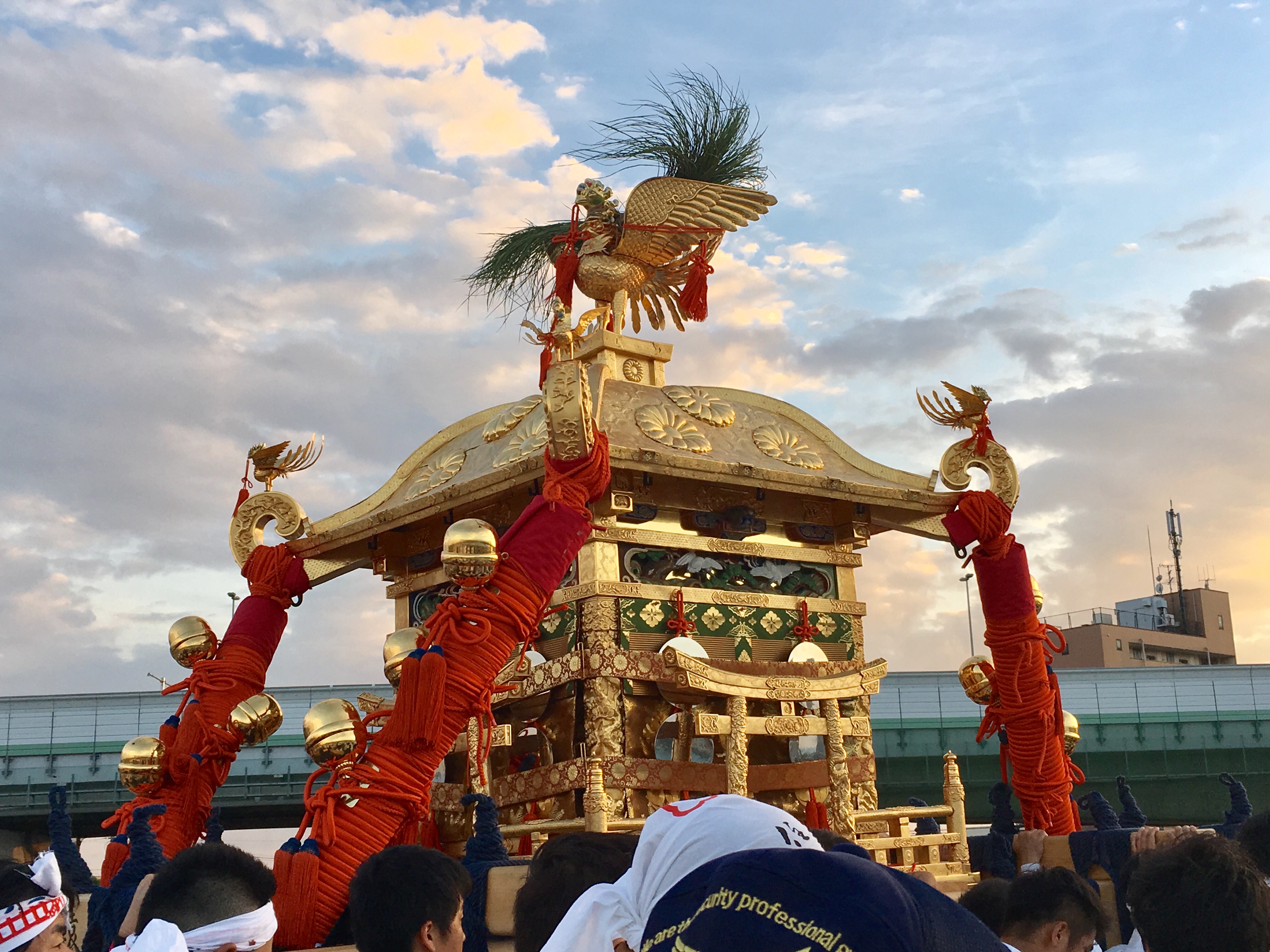 golden portable shrine with statue of large bird on top at sunset
