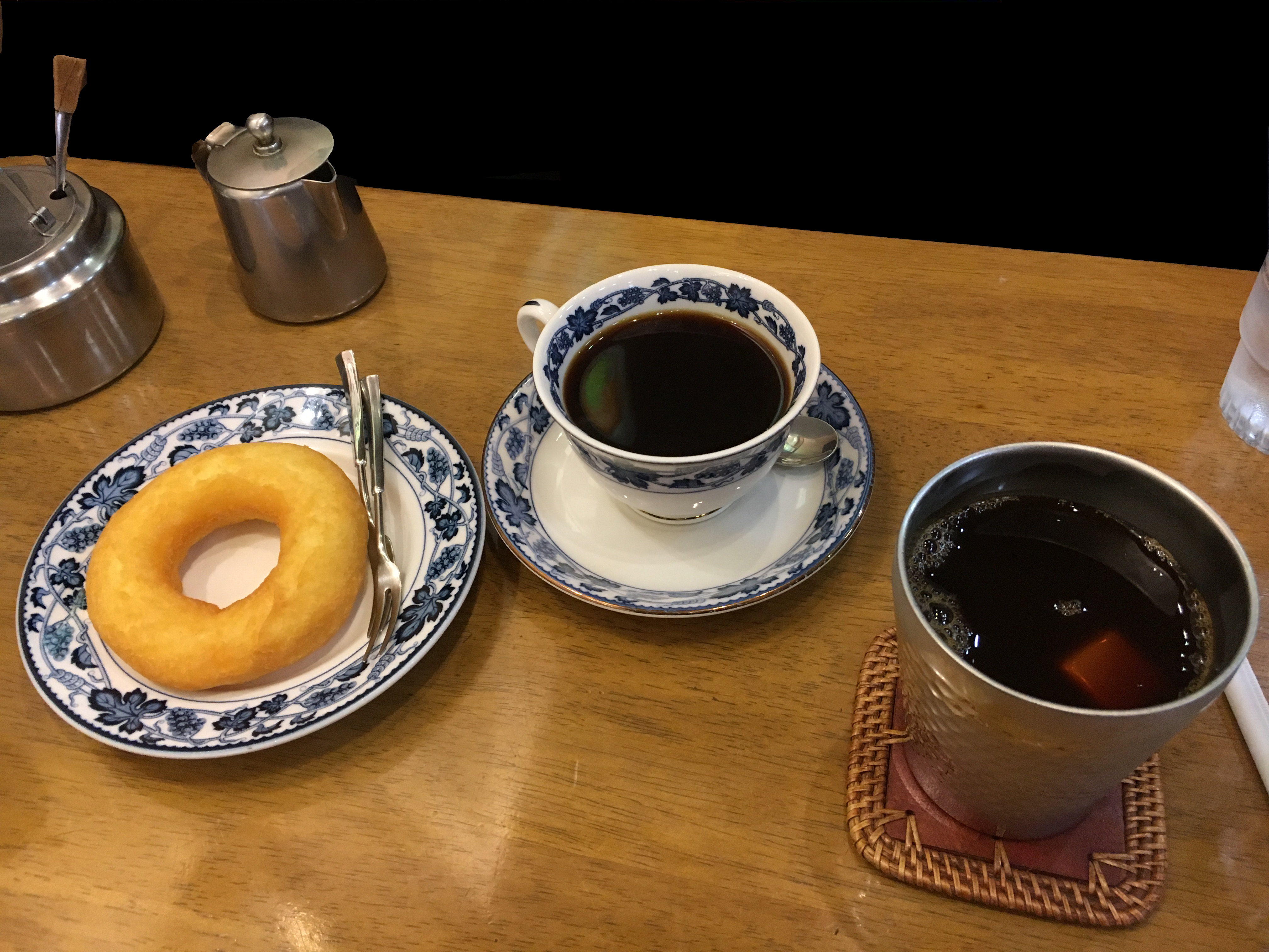two cups of coffee and a doughnut on a wooden table with sugar and cream