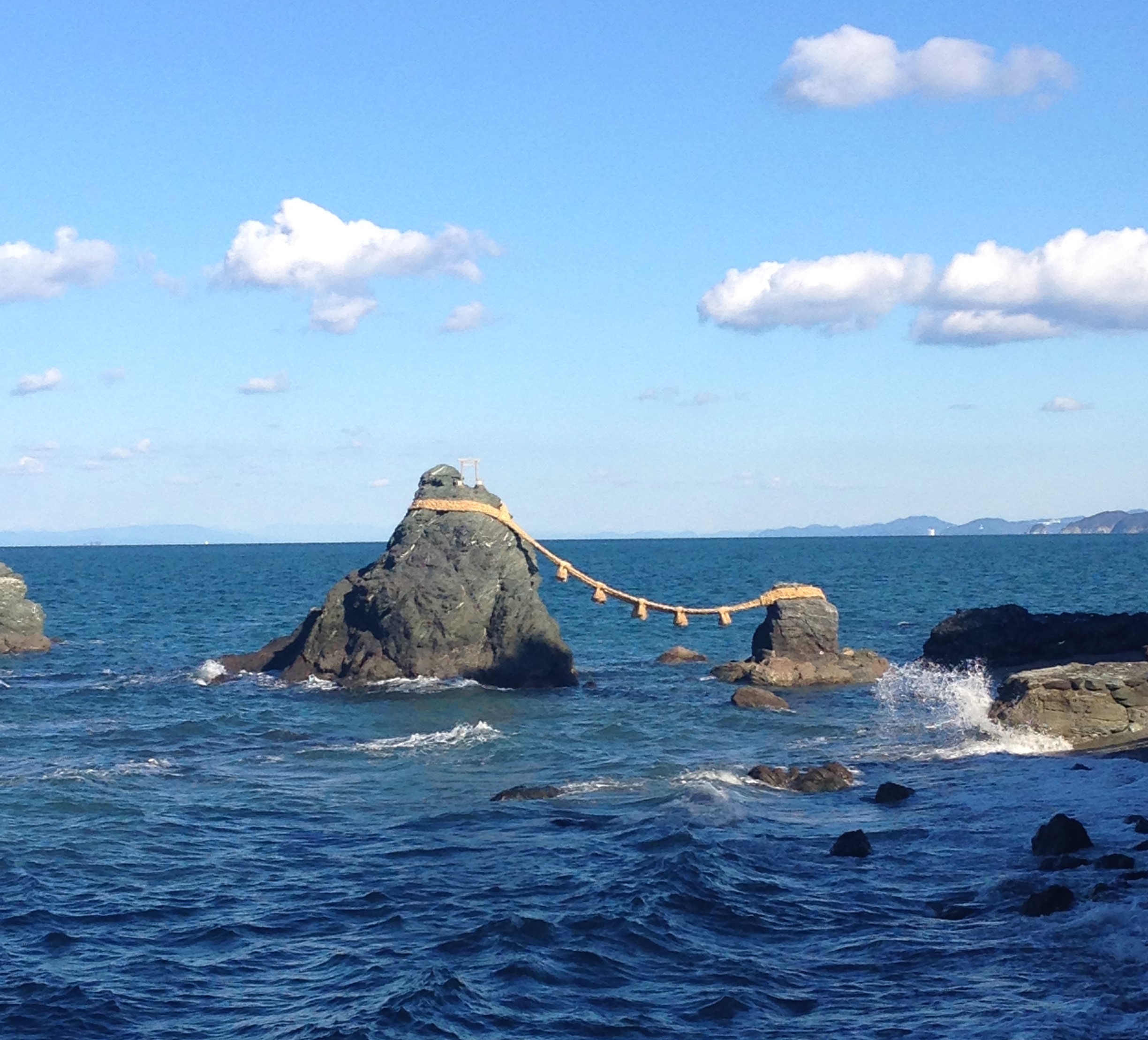 two large rocks connected by a long rope and a shrine on the taller rock in the blue sea