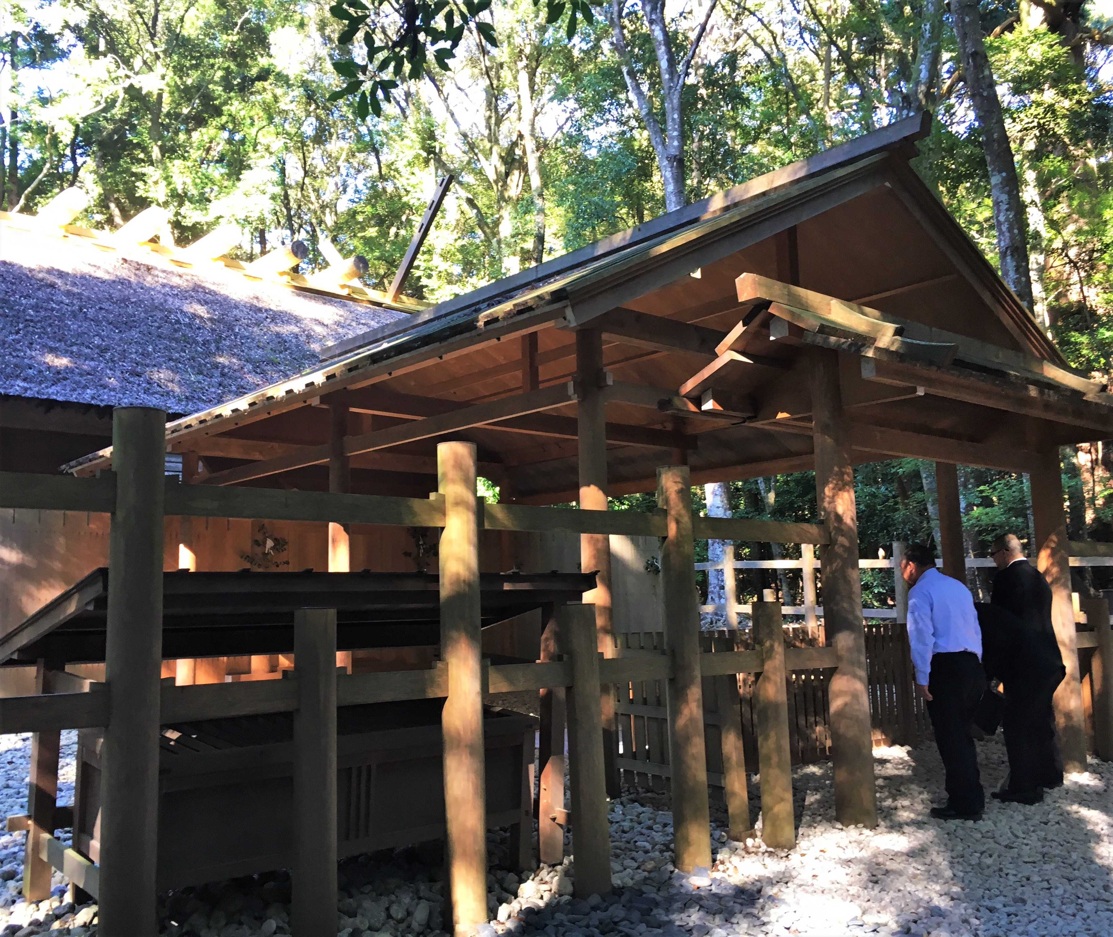 closeup of a wooden Japanese shinto shrine in the Naiku of Ise Jingu surrounded by trees and people praying