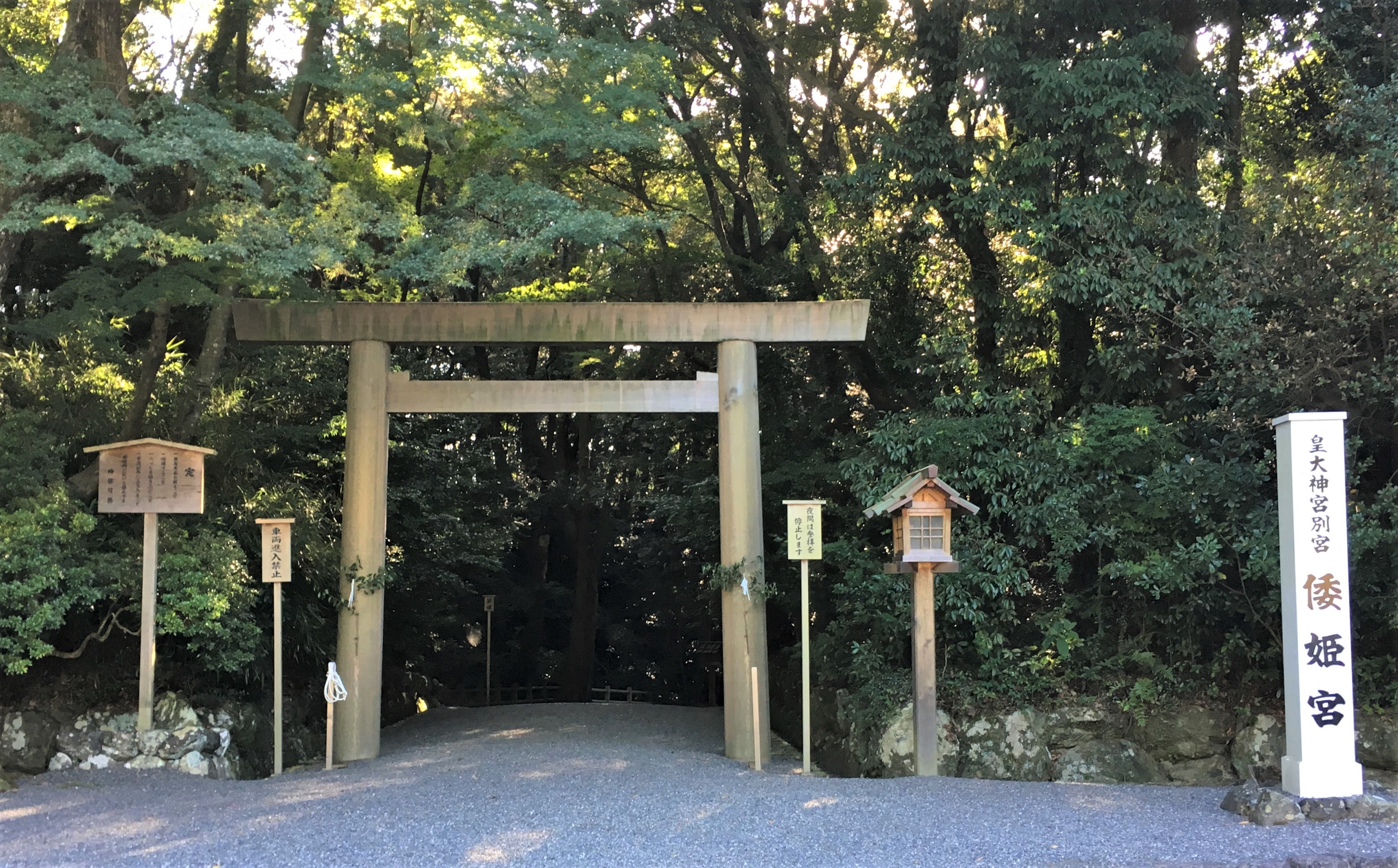Shinto shrine in a forested area gravel path and white marker that lists name of shrine
