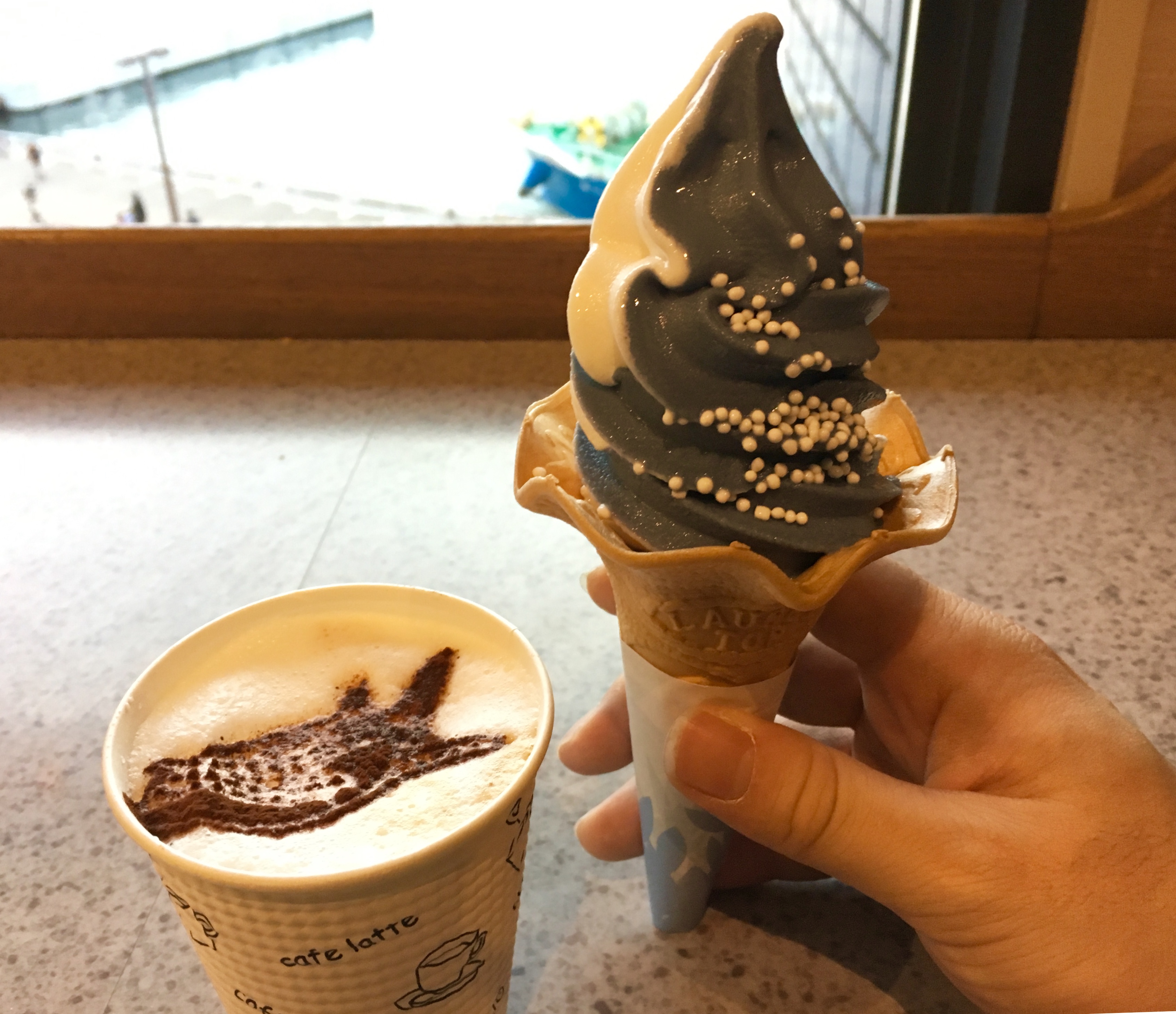 two toned cone of soft serve ice cream covered in white sprinkles and a coffee with whale shark latte art