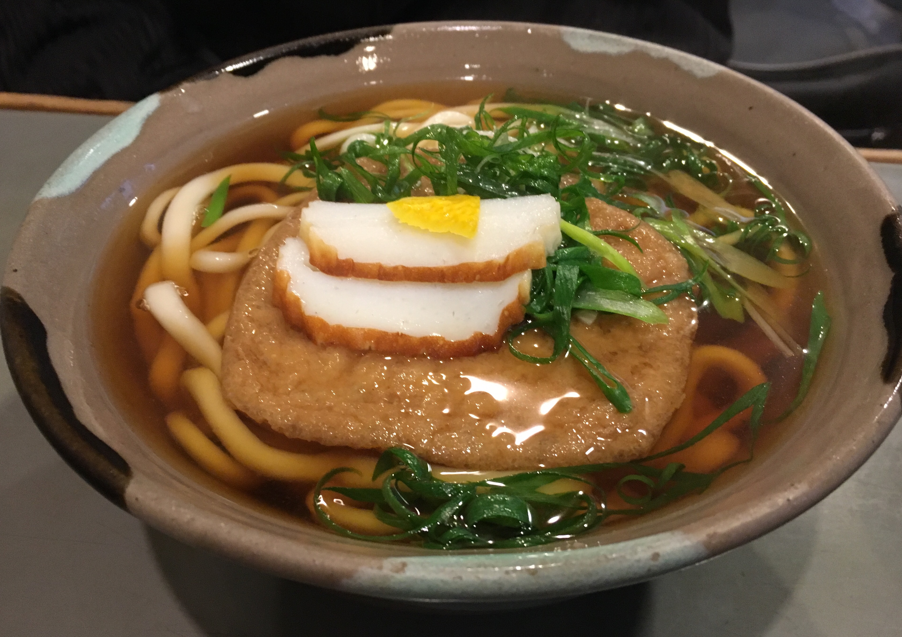 bowl of kistune udon topped with scallions kamoboko and yuzu peel