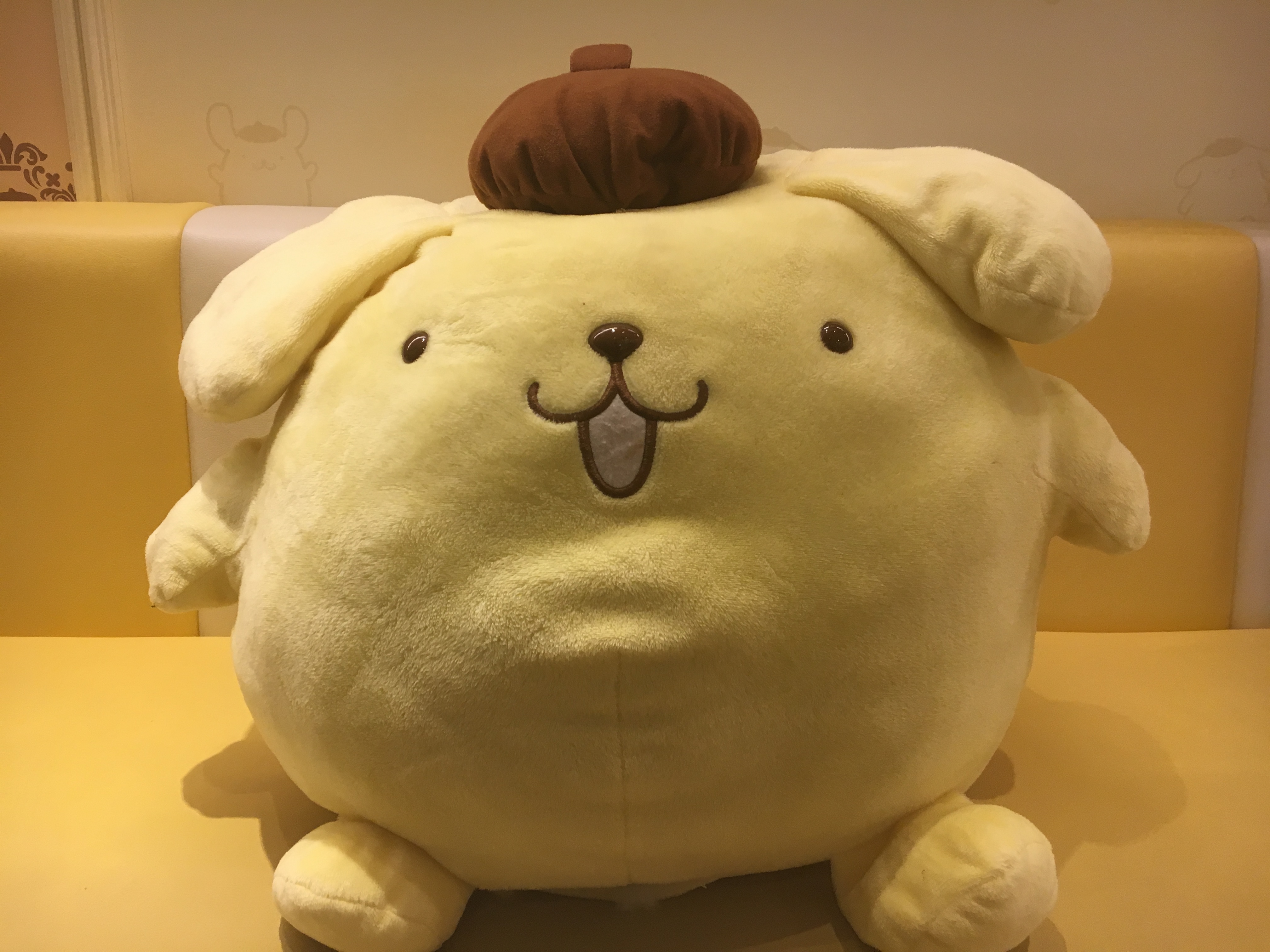 round plush doll of pompompurin on a yellow booth seat