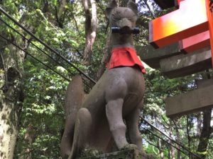 stone statue of a fox holding a scroll in its mouth at Fushimi Inari