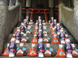 rows of small shite fox statues in formal Japanese clothing at Fushimi Inari Taisha