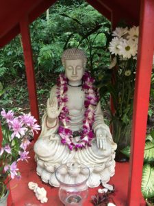 a statue of a buddha with an orchid lei in Hawaii's byodo-in temple